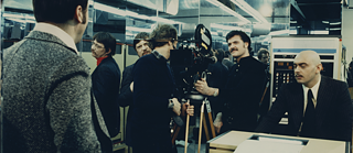 Fassbinder zusammen mit Schauspielern und einer Kamera beim Filmen des Films.