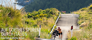 Eine Frau schiebt ihr Fahrrad über eine hügelige Straße in Italien.