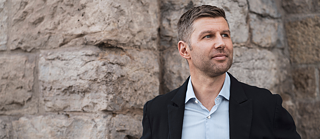 Porträt von Thomas Hitzlsperger in schwarzem Sakko und blauem Hemd, vor einer Wand aus Ziegeln