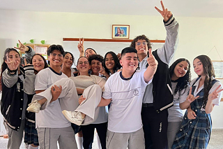 Jugendliche tragen eine junge Erwachsene, alle lachen.