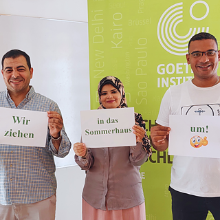 ثلاثة من زملائنا في فريق عمل معهد جوته بالغردقة يقفون سويا حاملين لافتات مكتوبة عليها نحن ننتقل