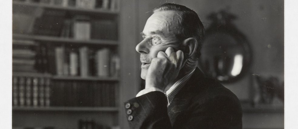 Томас Манн, портрет по груди, профіль ліворуч, сигара в правій руці, голова схилена на ліву руку, піднімає погляд від роботи.