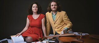 Die Pianistin Noémie Berz und der Cellist Kevin Bourdat sitzen auf dem Boden, vor ihnen verschiedene Bücher und ein Cello.