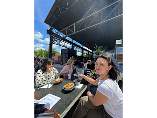 Einige Teilnehmende sitzen vor einer Bühne im Freien und essen zu Mittag 