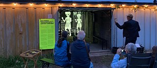 Im Vordergrund: Zwei Personen sitzen vor der Videoinstallation von Klaus Pobitzer in einer Garage der Ahornstraße in Chemnitz.