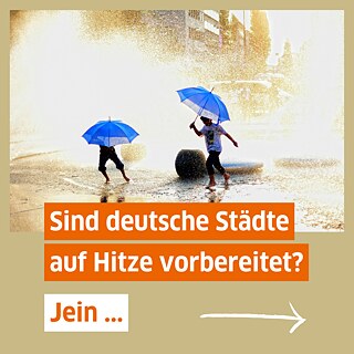 Spielende Kinder mit blauen Regenschirmen auf einem mit Wasser besprühten Platz