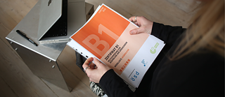 Blick von oben auf eine Deutschlehrerin, die ein Goethe-Zertifikat B1 in der Hand hält.