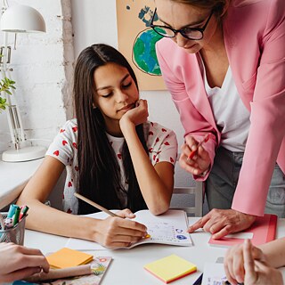 Eine Frau hilft zwei Mädchen bei den Hausaufgaben und fördert dabei ihr Lernen und Verständnis des Stoffes