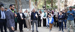 منسق المشروع يتحدث في ميكروفون وسط مجموعة من الزوار خلال معرض في معهد غوته بالدقي.