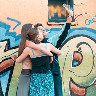 Drei junge Frauen machen ein Selfie vor einem Graffiti mit der Aufschrift ‚Change‘