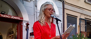 Die Autorin Susanne Franz bei einer Lesung im Freien. Vor ihr steht ein Mikrofon und sie hält ein Buch in den Händen, aus dem sie vorliest.