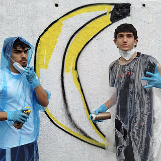 Zwei Jugendliche sprühen ein Graffiti auf eine weiße Wand.