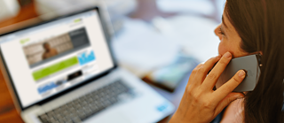 A woman is talking on the phone in front of her laptop.