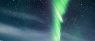 Vivid green and white Northern Lights stretch across a starry sky.