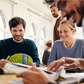 A gathering of people around a table, smiling and interacting as they share thoughts and experiences together