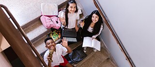 A trio of young individuals with backpacks relax on stairs, engaged in conversation and laughter