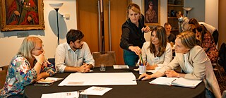 A gathering of people around a table, smiling and interacting as they share thoughts and experiences together