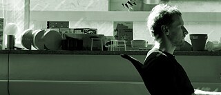 Man sieht einen Mann von der Seite, der an einem Schreibtisch sitzt.