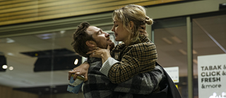 Ein Mädchen und ein Junge starren sich an, während sie etwas aus dem Kühlschrank eines Geschäfts nehmen. 