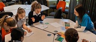 Students collaborating and sharing ideas at a table in a lively classroom environment
