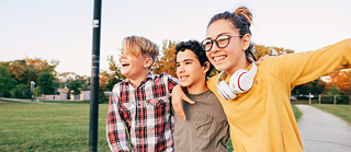 Drei Kinder sind im Freien und umfassen sich an den Schultern während sie in die Luft hüpfen