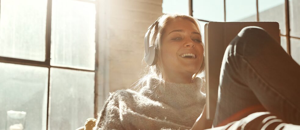 Mlada žena sa slušalicama komunicira s nekim putem tableta i smeje se.