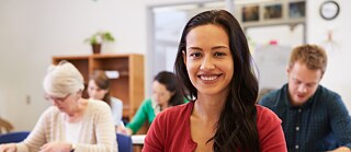 Unterrichtsraum mit einer Schülerin vorne und andere Schüler*innen in Hintergrund