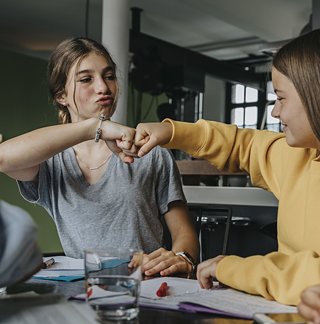 Zwei Teenager fistbumping beim Arbeiten im Klassenraum. 