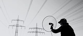 Klangkünstler Lasse-Marc Riek zeichnet Töne auf. Im Hintergrund sind Strommasten zu sehen.