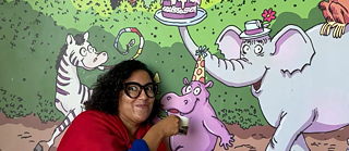 A woman with short hair wearing a red coat pointing at an animated painting.