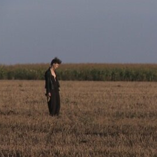 Weitwinkelaufnahme einer Frau, die auf einem Feld steht und auf den Boden schaut