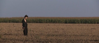 Weitwinkelaufnahme einer Frau, die auf einem Feld steht und auf den Boden schaut