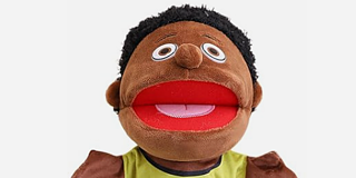 Eine dunkelbraune, männliche Sprechpuppe, die eine blaue Hose und ein gelbes T-Shirt trägt. 