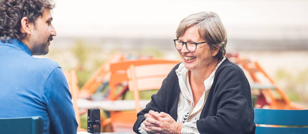 Sur la photo, on voit Jenny Erpenbeck assise dans le jardin, souriante, face au journaliste.