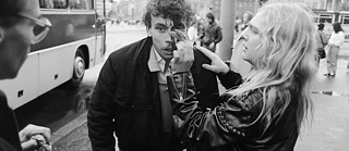 La photo montre un homme, portant une veste en cuir, qui efface du sang du visage d'un autre homme, à l