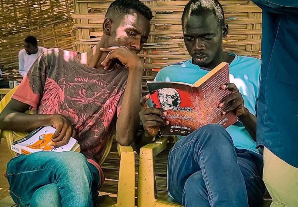 Two Sudanese men are reading books.
