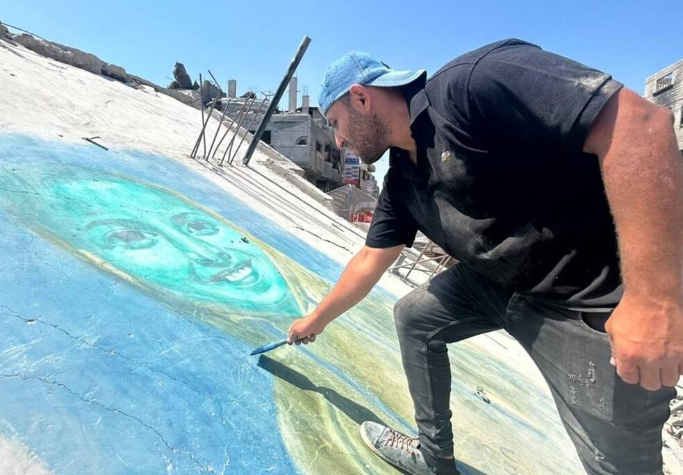 رجل يرتدي قبعة يرسم وجهًا مبتسمًا على حطام المباني التي تعرضت للقصف.