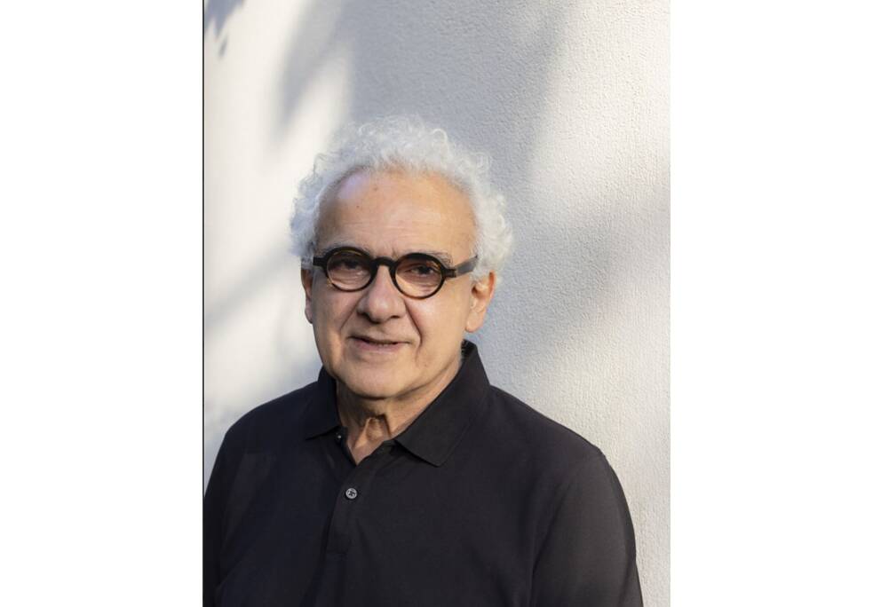 Ein alter Mann mit Brille steht vor einer weißen Wand