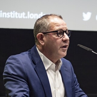 John Kampfner giving a speech with microphone infront 