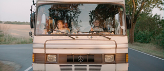 Frontalansicht von zwei jungen Menschen, die in einem alten Mercedes-Camper fahren.