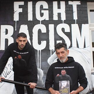 L'image montre 2 personnes devant un tag qui dit "Fight racism"