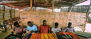 a group of Sudanese men are sitting and reading books.