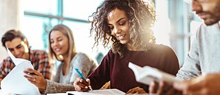 Vier junge Menschen lesen lächelnd aus Büchern und Arbeitsblättern