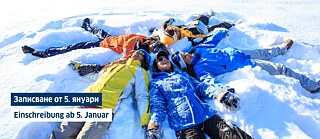 Eine Gruppe junger Leute liegt lachend auf dem Rücken im Schnee. Sie bilden einen Kreis, halten sich an den Händen und formen Schnee-Engel.