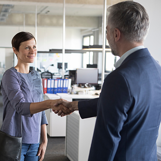 Two professionals shaking hands in an office environment, symbolizing a successful business meeting or agreement.