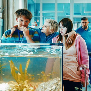 Das Foto zeigt drei Personen vor einem Aquarium und im Hintergrund eine Person stehend.