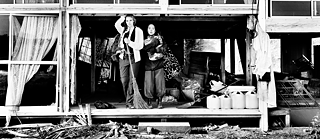 Das Foto zeigt zwei Personen in einem schwarz-weiß Bild. Beide stehen und blicken in die Kamera und eine Person hält einen Besen in der Hand.