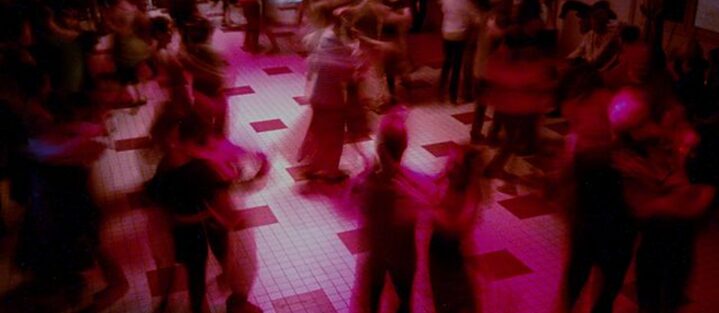 Es ist ein Ballsaal in rosa Licht zu sehen, in dem viele Paare tanzen