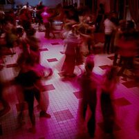 Es ist ein Ballsaal in rosa Licht zu sehen, in dem viele Paare tanzen