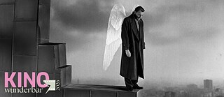 Das schwarz-weiß Bild zeigt eine Person auf einer hohen Mauer stehend im Engelsflügel im Nebel. Im Hintergrund und weitentfernt sieht man die Skyline der Stadt